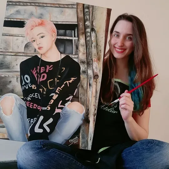 Fabiana sorrindo, com um pincel na mão, ao lado de uma pintura